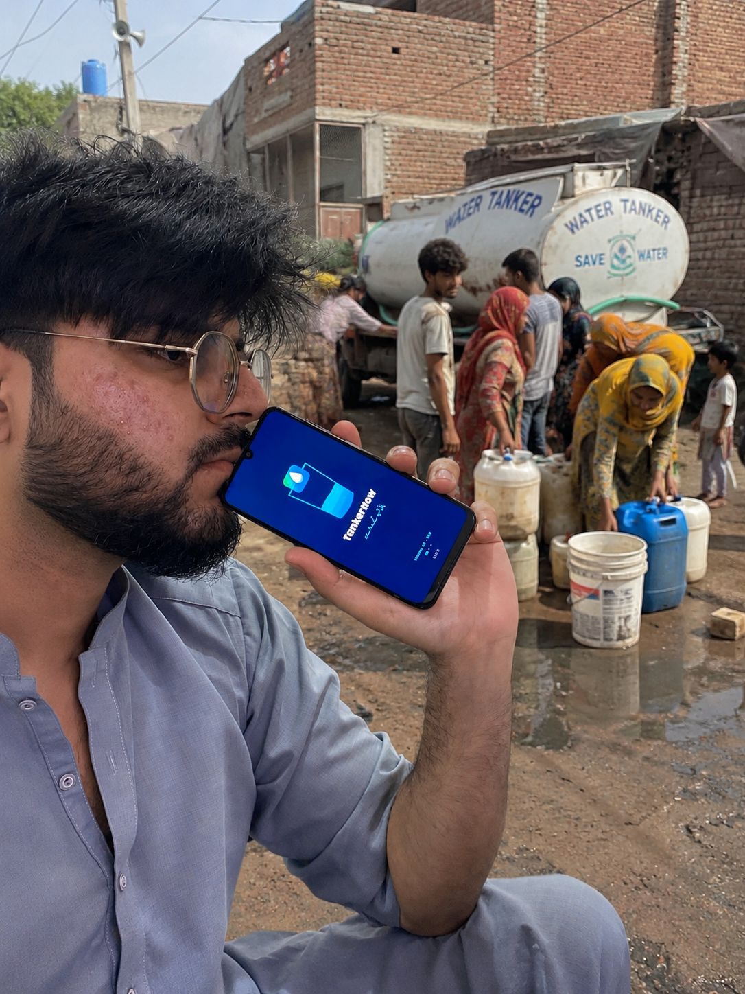 Muhammad Rohail holding TankerNow app at a water tanker filling scene
